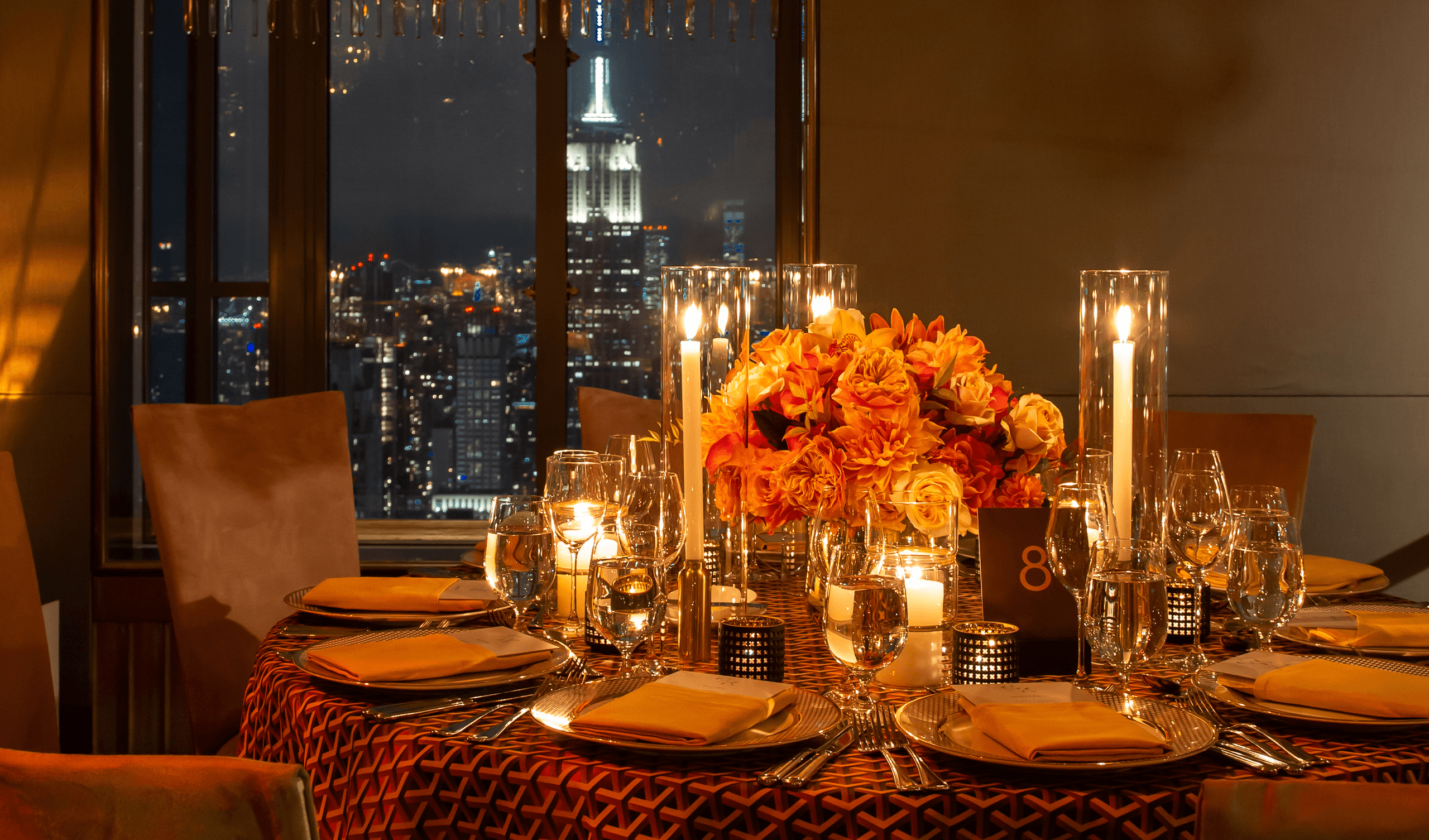 Elegant modern wedding tablescape with candlelight, orange flowers and city skyline view
